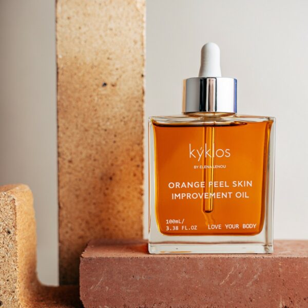 A bottle labeled "Kyklos Orange Peel Skin Improvement Oil" with a dropper, up to a brick, embodies the essence of natural cosmetics aimed at improving skin texture and reducing the appearance of cellulite.