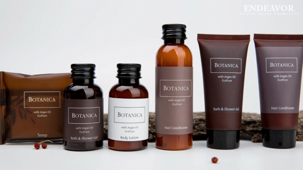 An elegant display of luxury hotel toiletries brand Botanica. Mini bottles of shower gel body wash, body lotion, hair conditioner, a soap bar wrapped in bag and shower gel, body wash, hair conditioner in mini tubes.